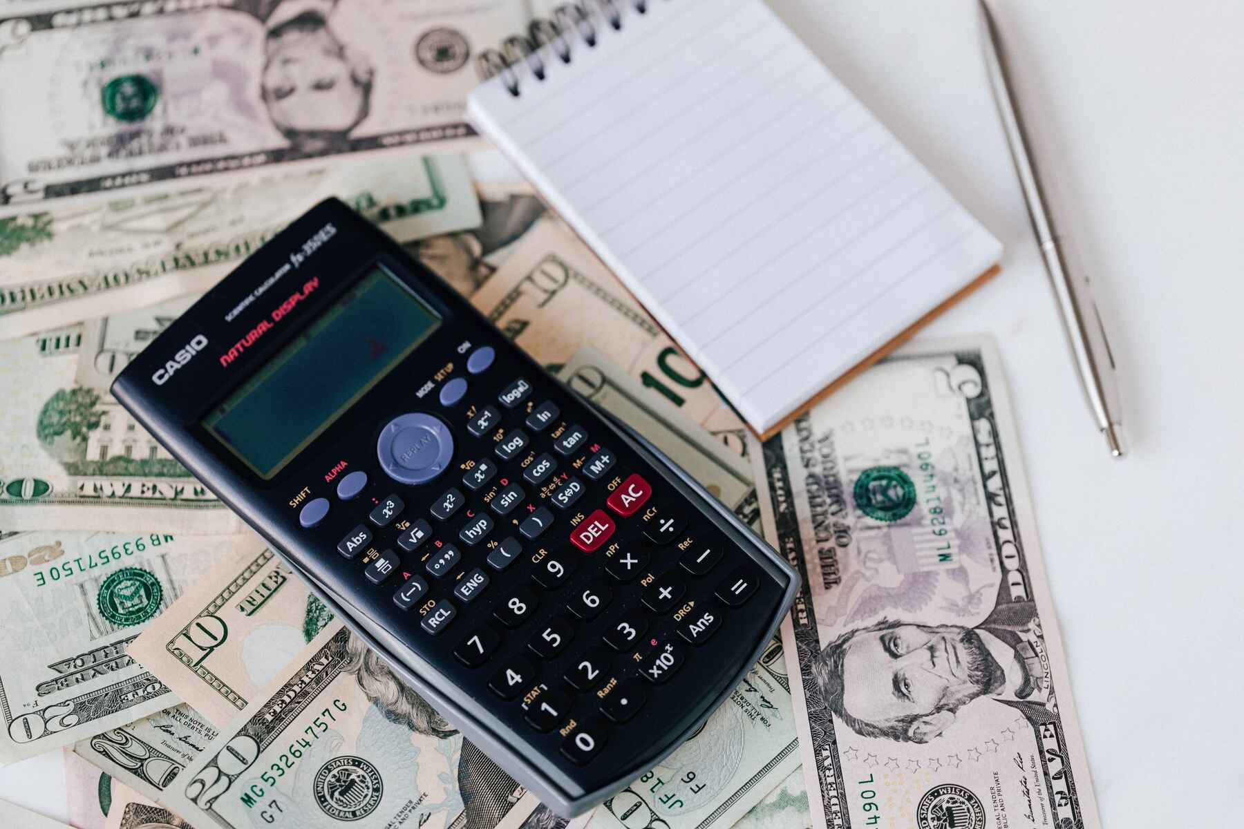 Calculator and notepad on top of dollar bills on the table