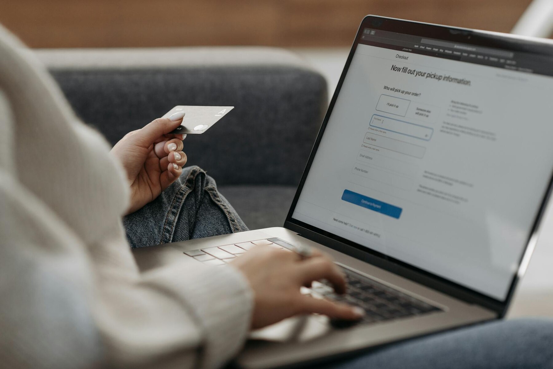 A close-up of a hand holding a credit card while shopping online on a laptop