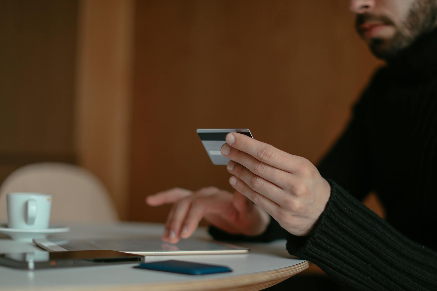 A man holding a credit card and tapping on a smartphone at a café table