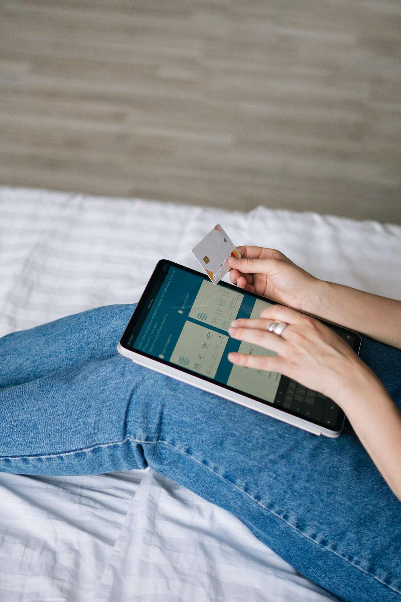 A person holding a credit card while using a tablet on a bed