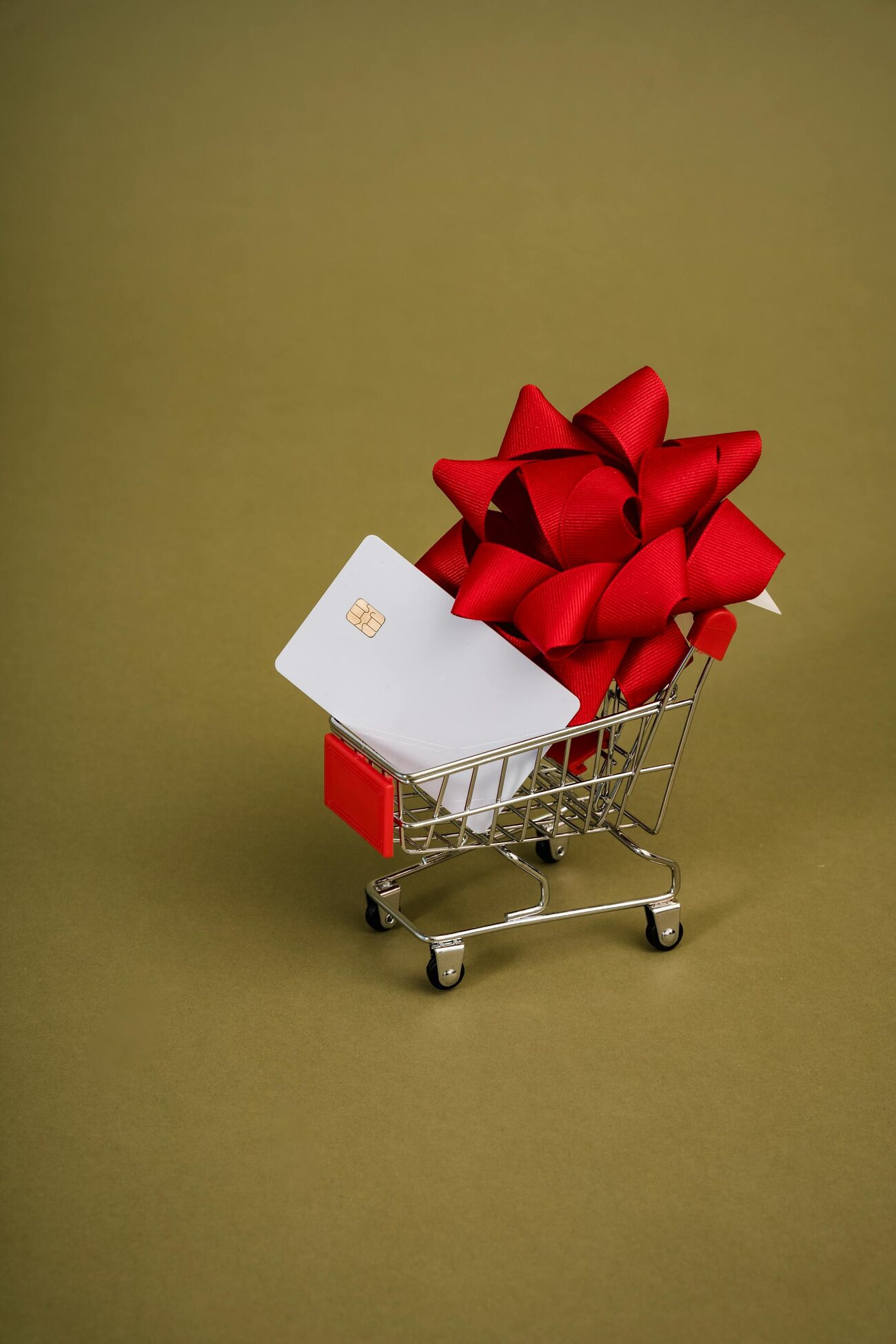 A credit card with a red bow in a miniature shopping cart on a green background