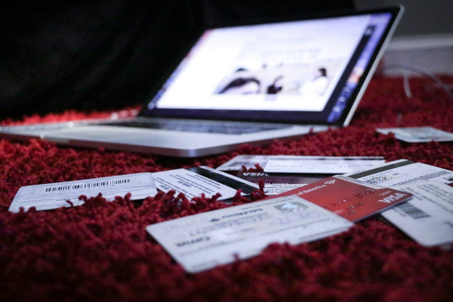 Credit cards scattered on a red carpet with an open laptop in the background