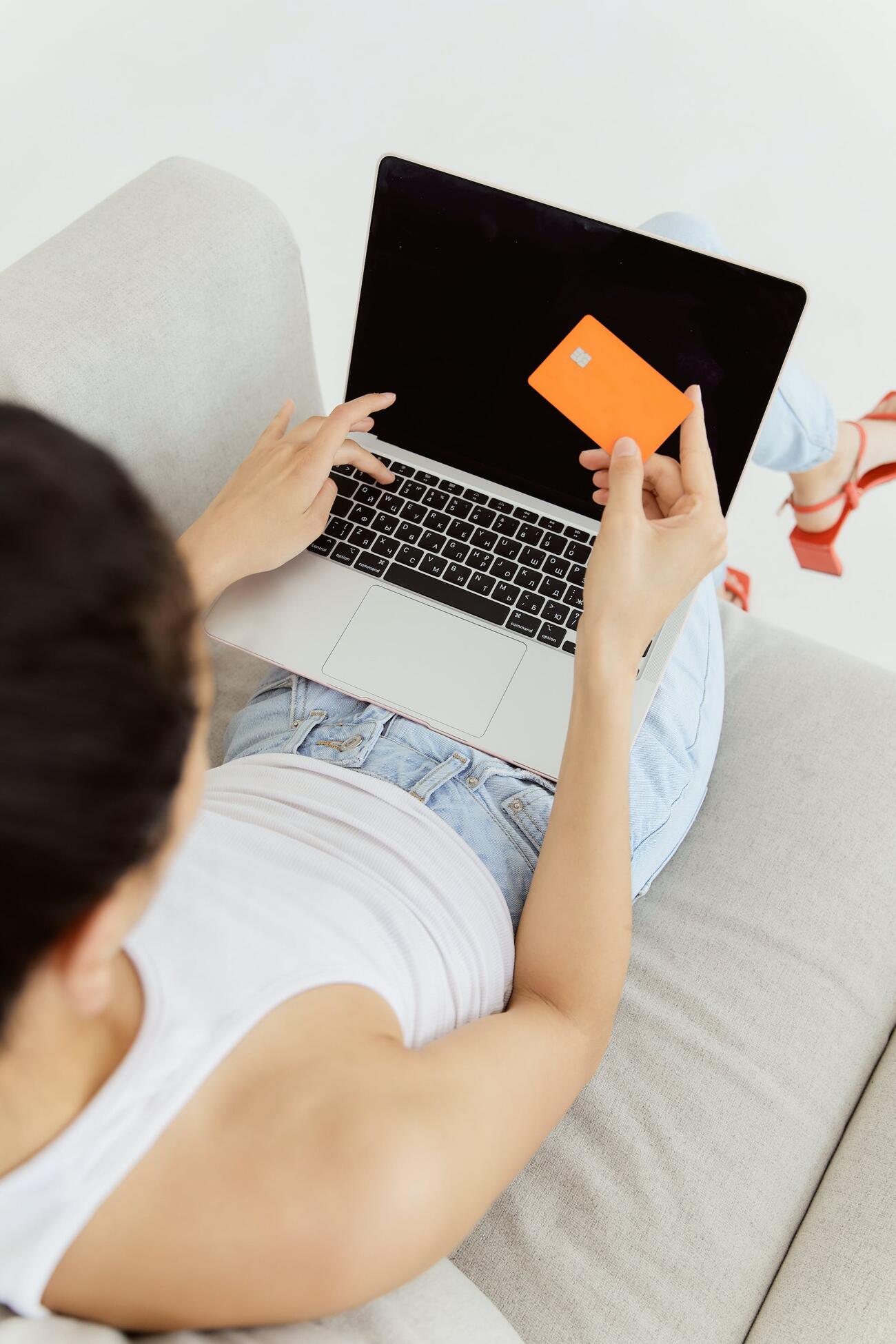 A woman sitting on a couch holding a credit card while typing on the laptop on her lap