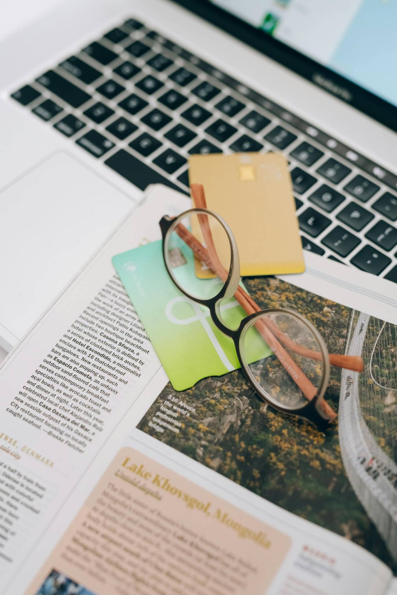 Eyeglasses, credit cards, and an opened page of a magazine on top of a laptop