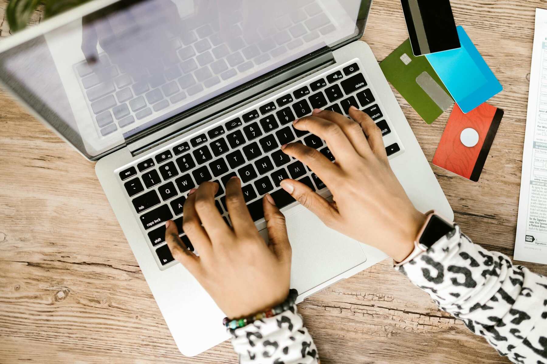 A woman's hands on a laptop, surrounded by credit cards and other items