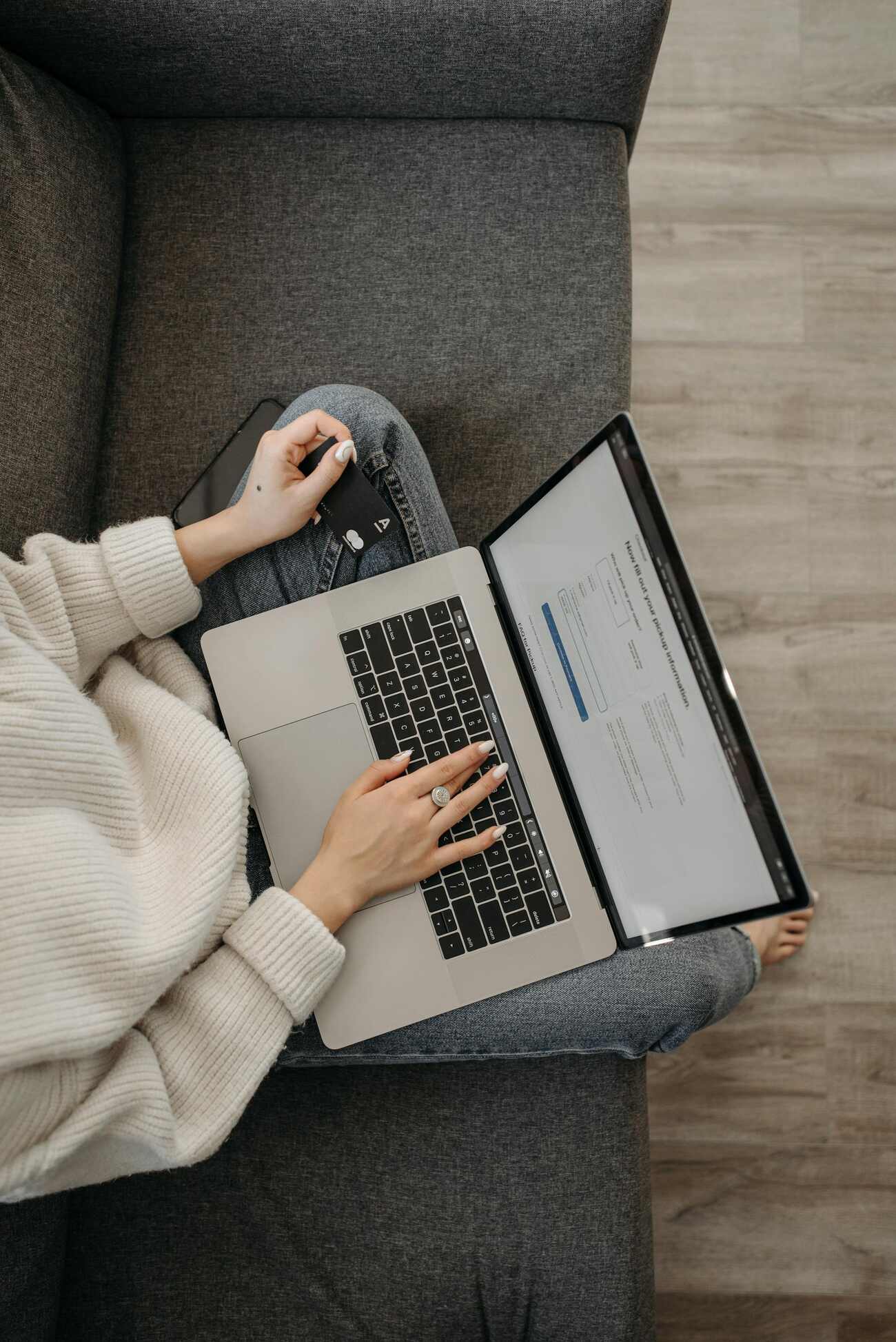 A woman sitting on a couch with a laptop and a credit card