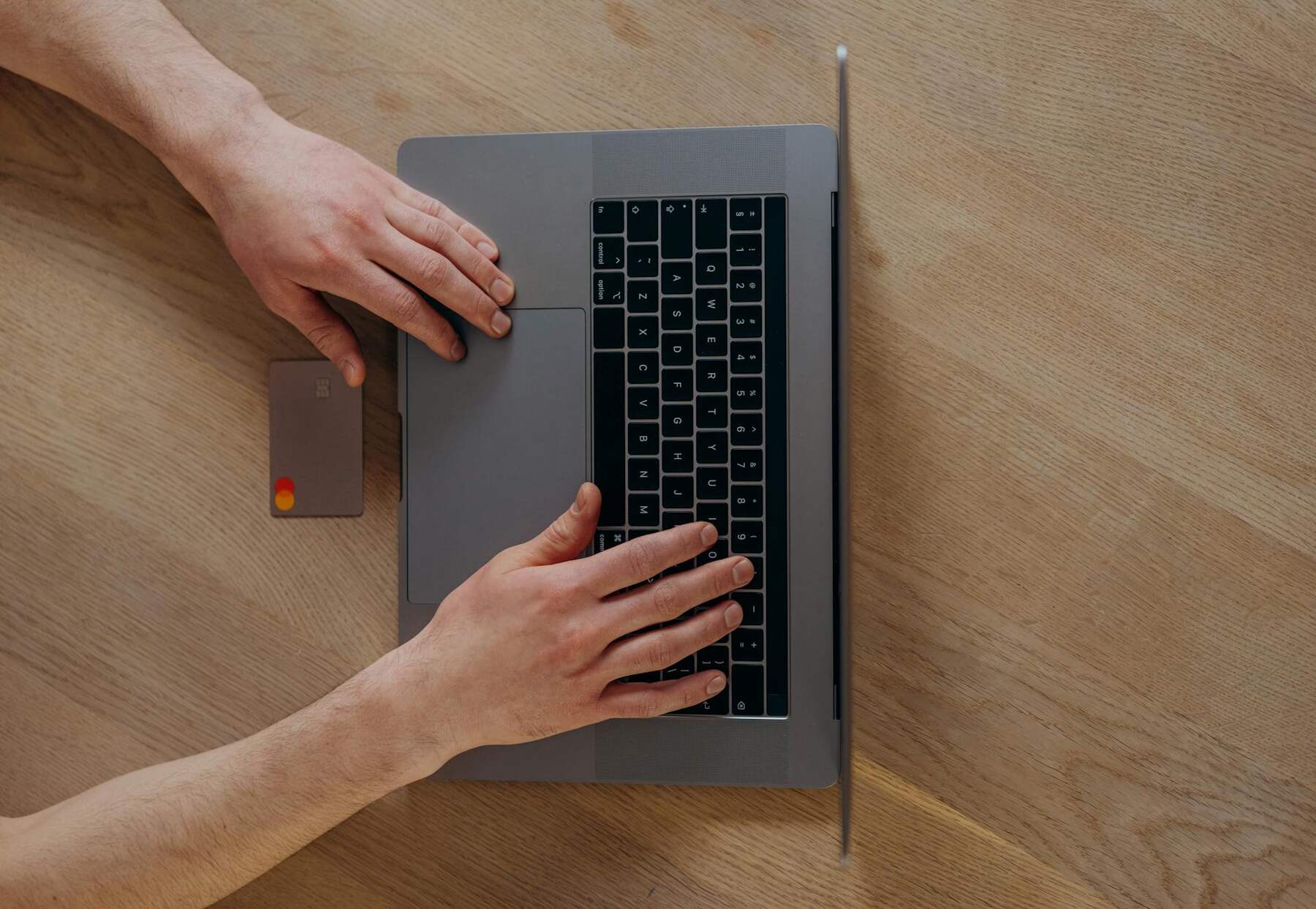 A man typing on a laptop with a credit card  near the touchpad