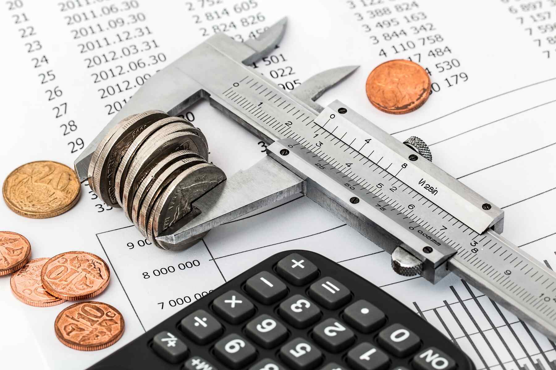 Caliper holding coins on top of a printed paper and beside a calculator