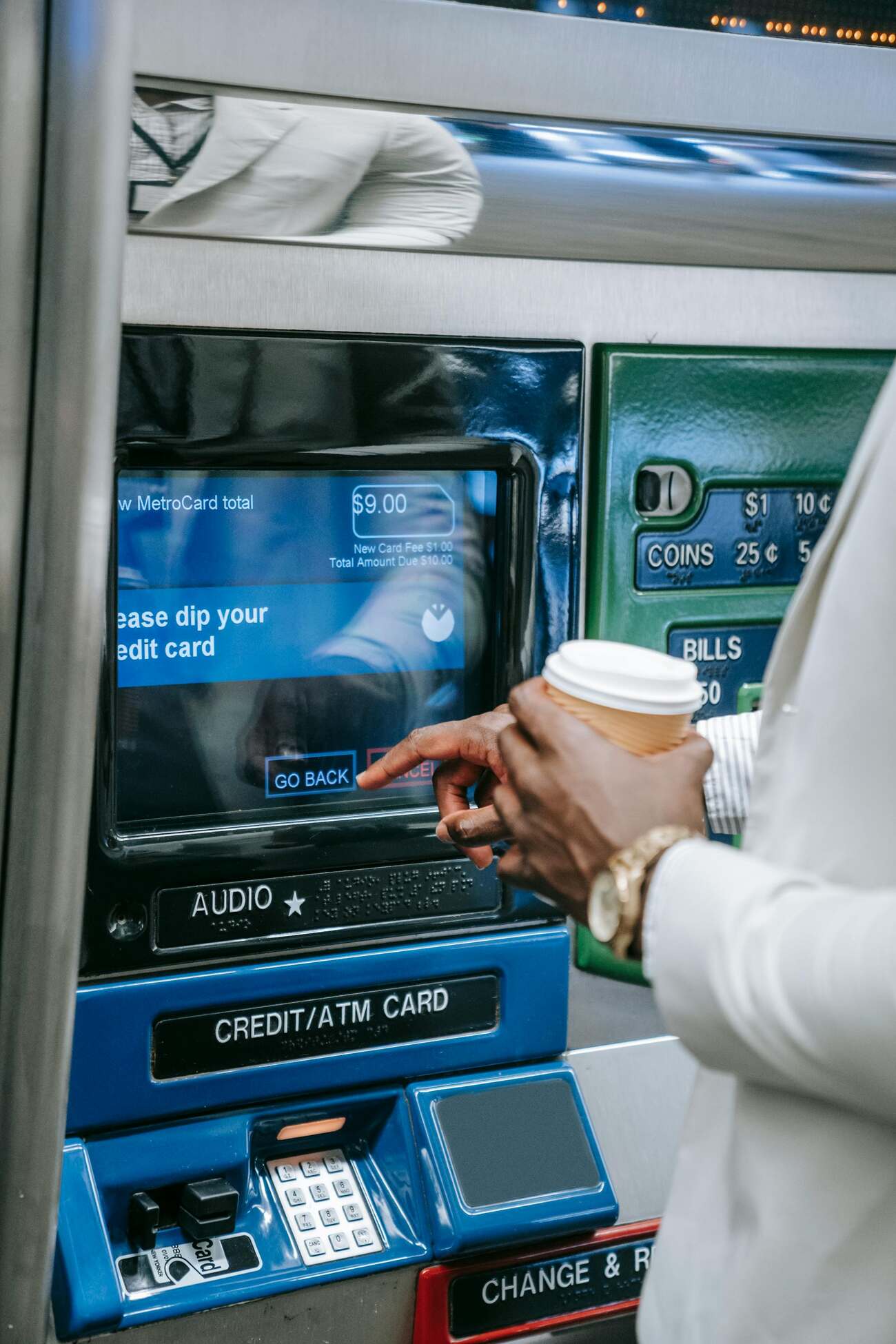 A man at an ATM machine holding a cup of coffee