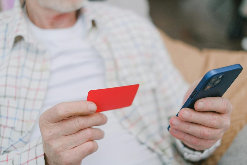 An older man with a red credit card and a cell phone in hand
