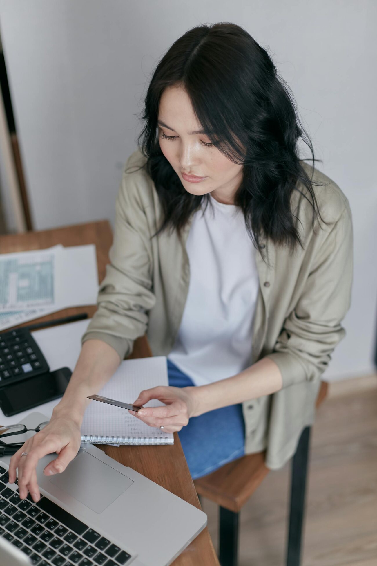 A woman focused on her laptop, sitting at a desk while holding a credit card