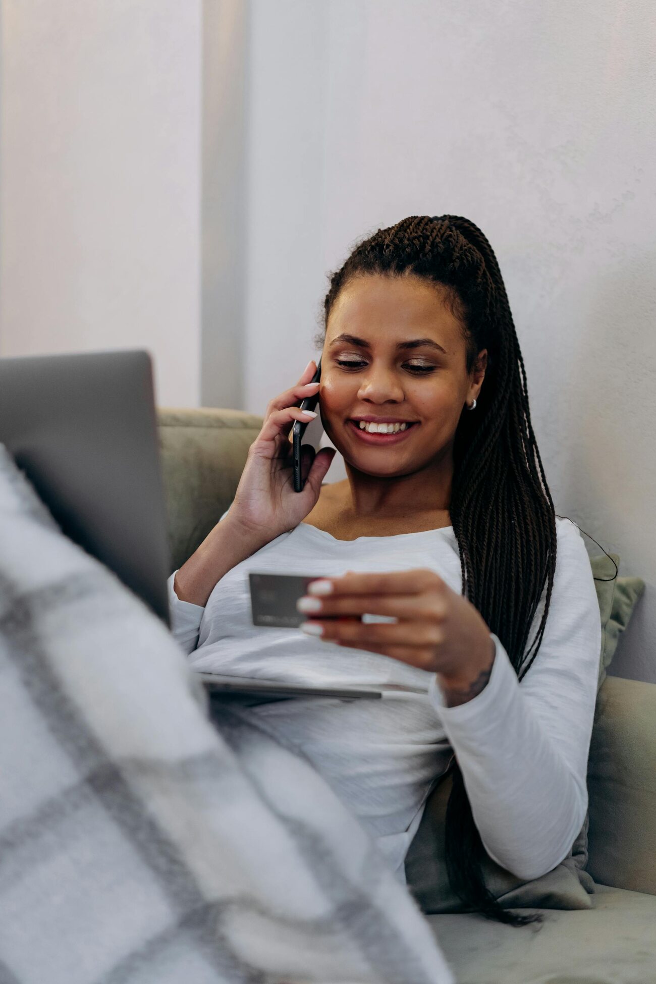 A woman sitting on a couch, holding a credit card and a laptop on her lap