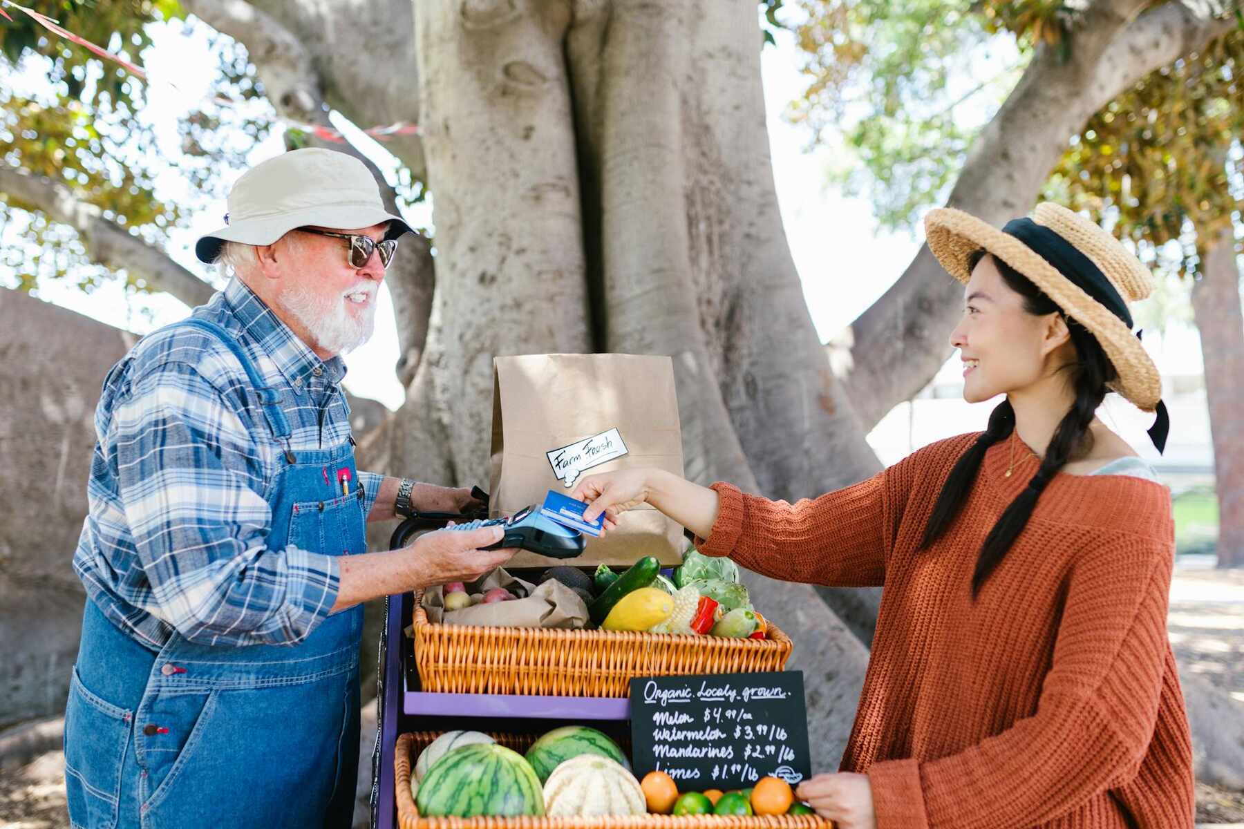 A man and woman with a variety of produce in front of a tree