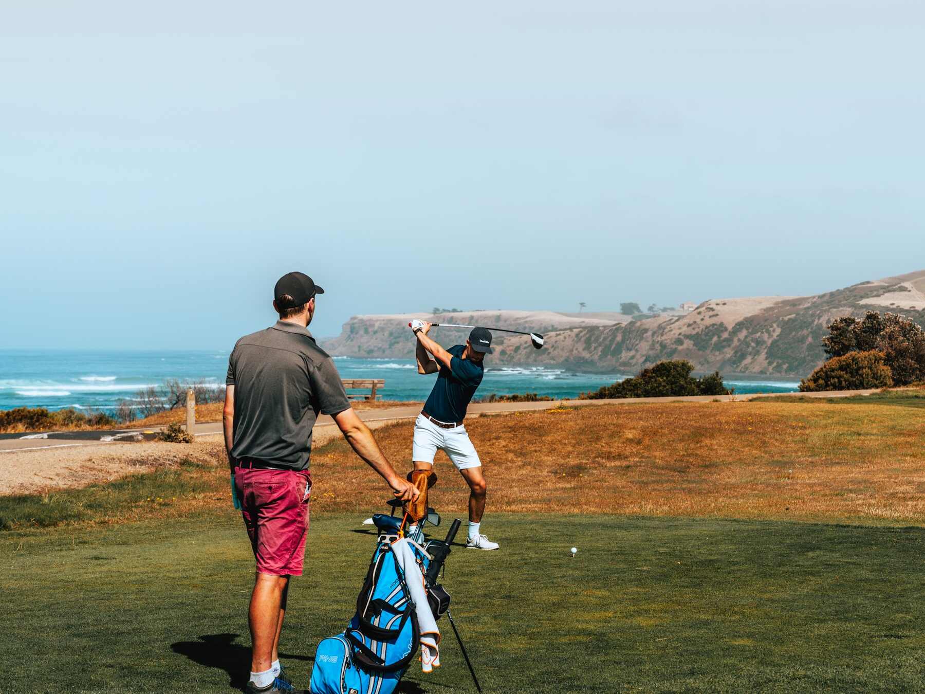 Two men playing golf on a sandy beach