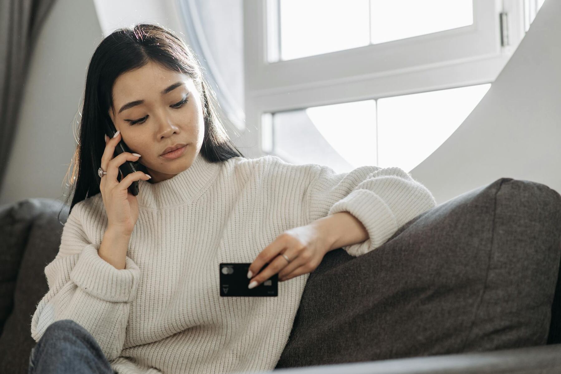 Woman sitting on couch, holding credit card and mobile phone