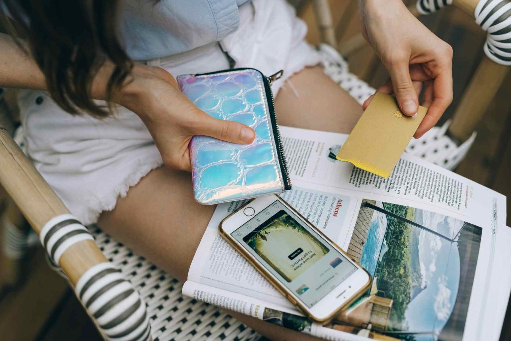 A woman holding her card while looking at a magazine and phone