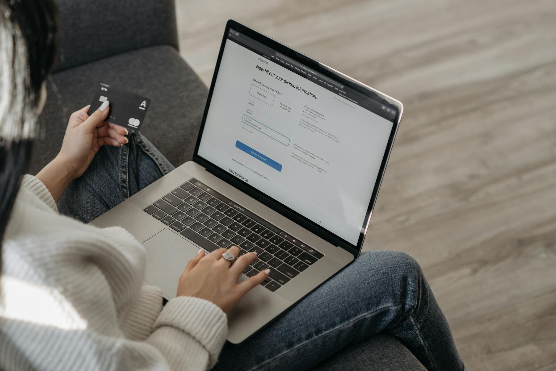 A woman sitting on a couch holding a credit card, engrossed in her laptop