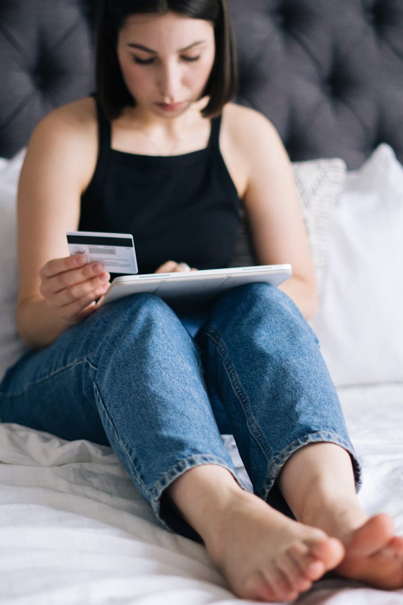 A woman relaxing on a bed, feet up, holding a credit card and tablet