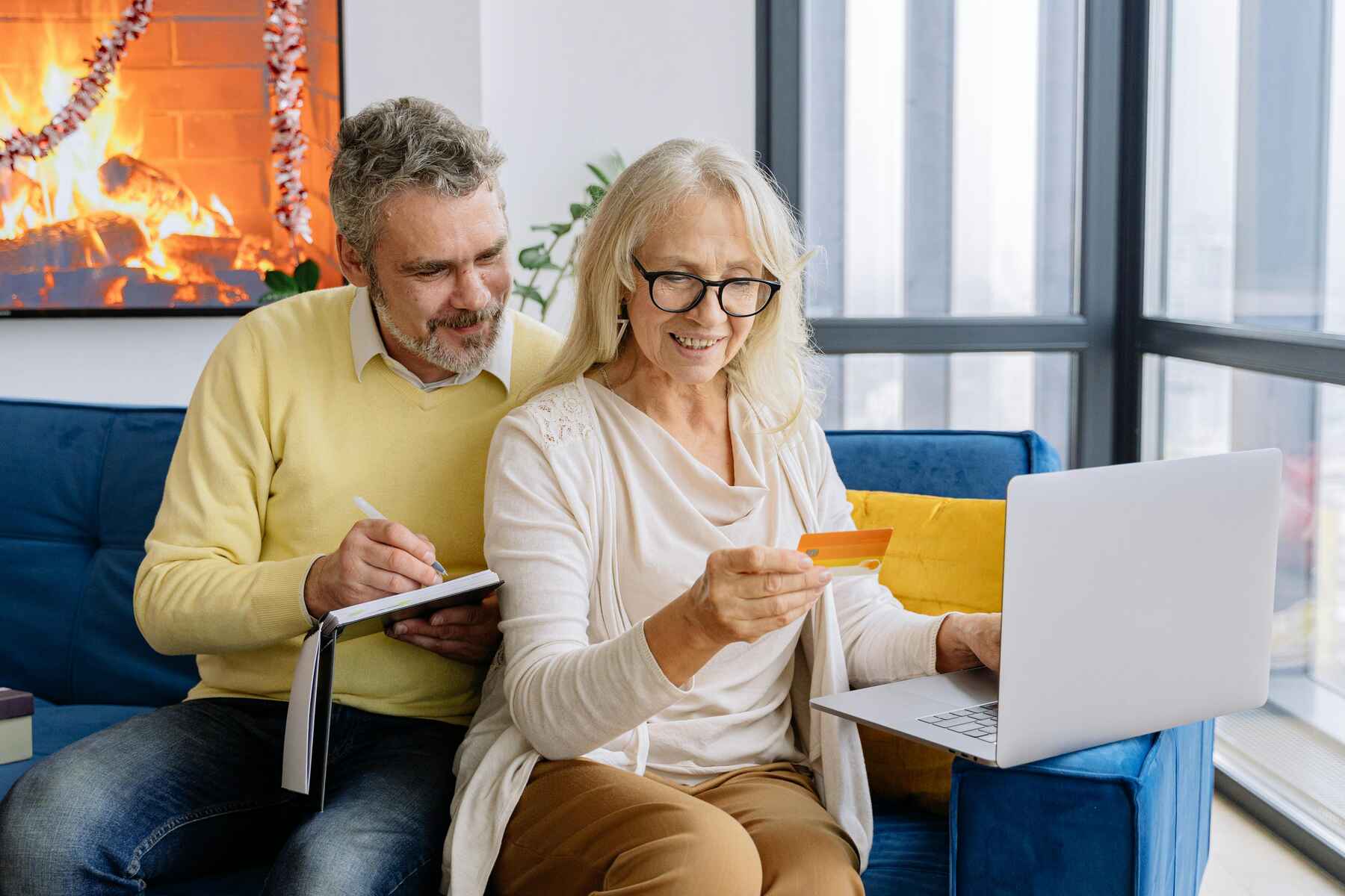 A man writing notes while his wife holds a card and laptop