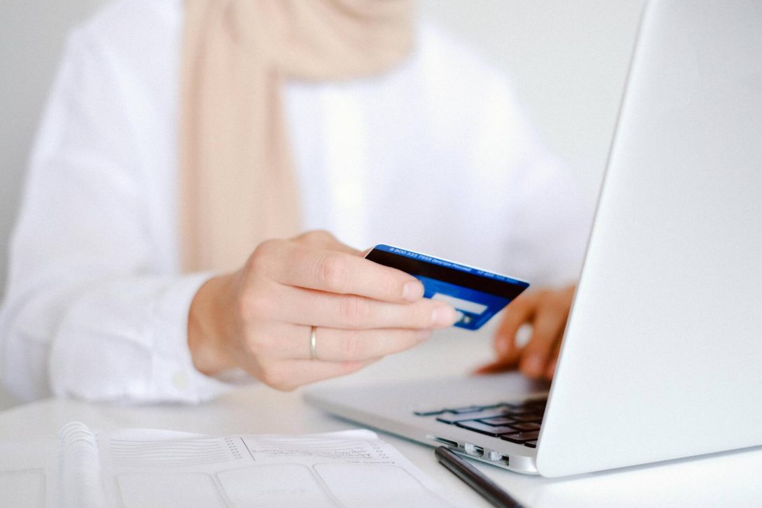 A woman holding a blue credit card while typing on the laptop