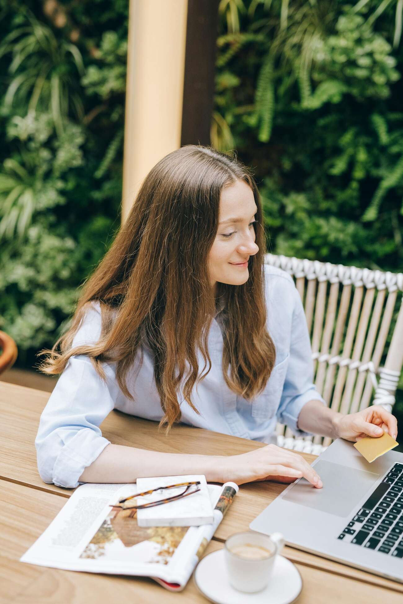 A lady holding a credit card while browsing with her laptop outdoors