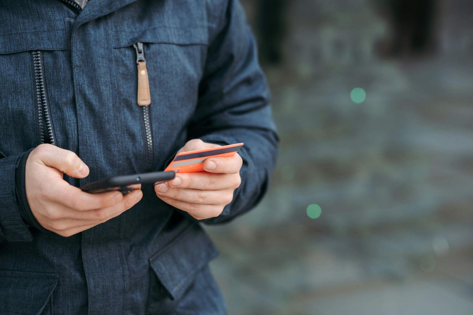 A man holding an orange credit card and a phone