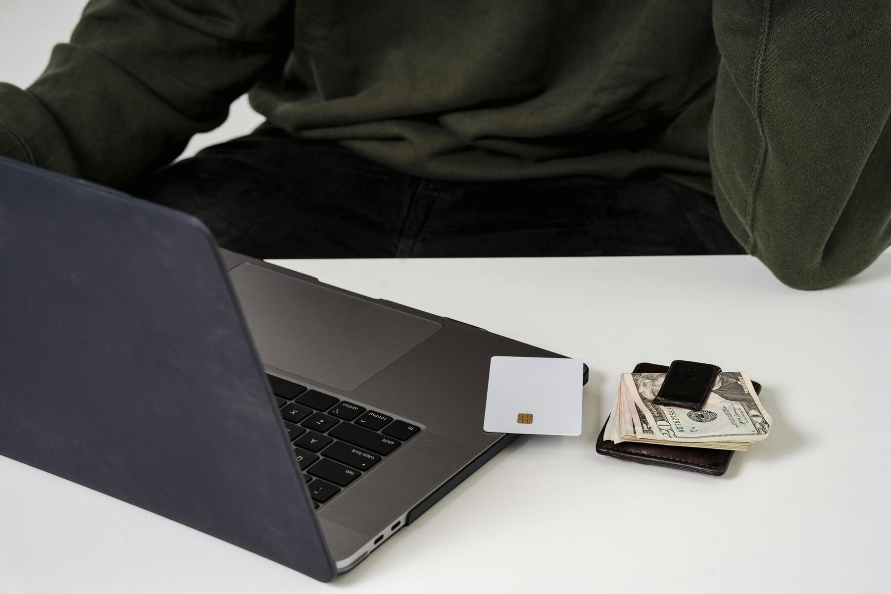 A credit card on the laptop with bills and a wallet beside it