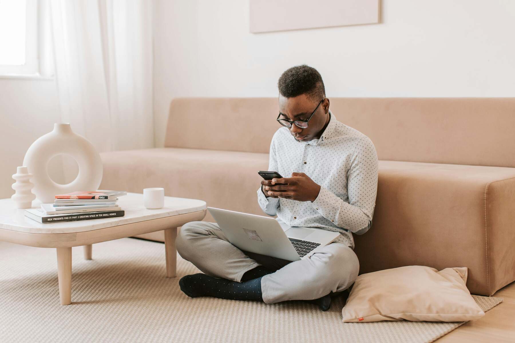 A student sitting on the living room using his phone and his laptop open